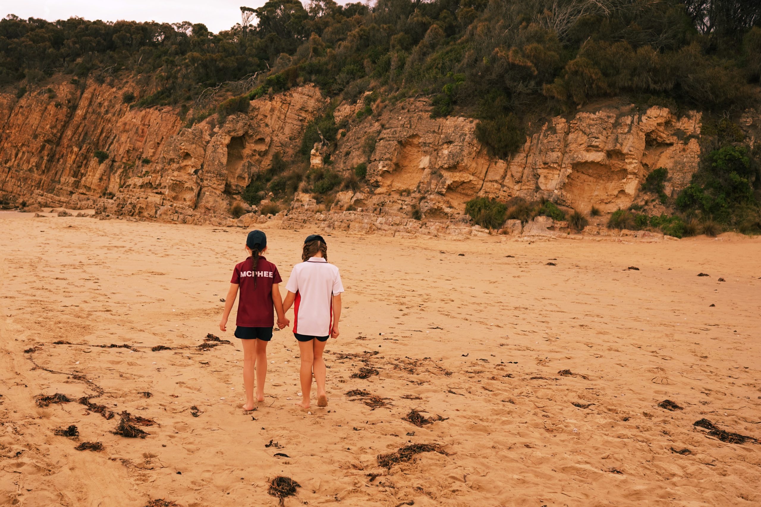 Collegiate girls walking along a beach, holding hands