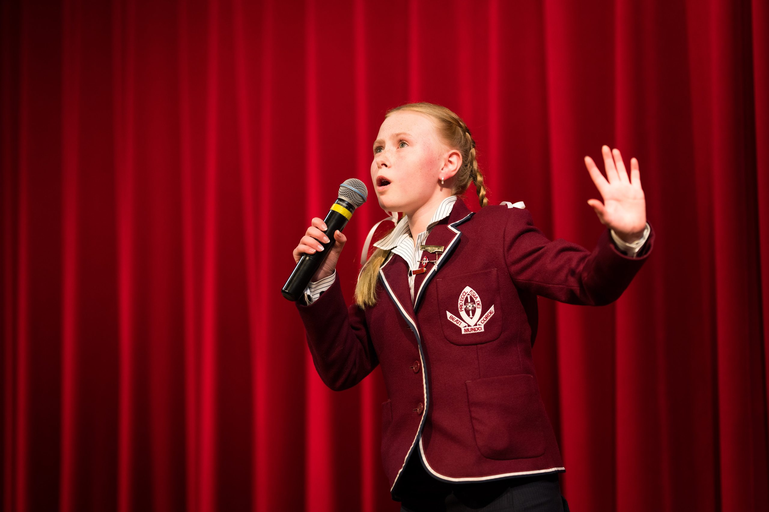 Middle School student singing into microphone with stage curtains behind her.