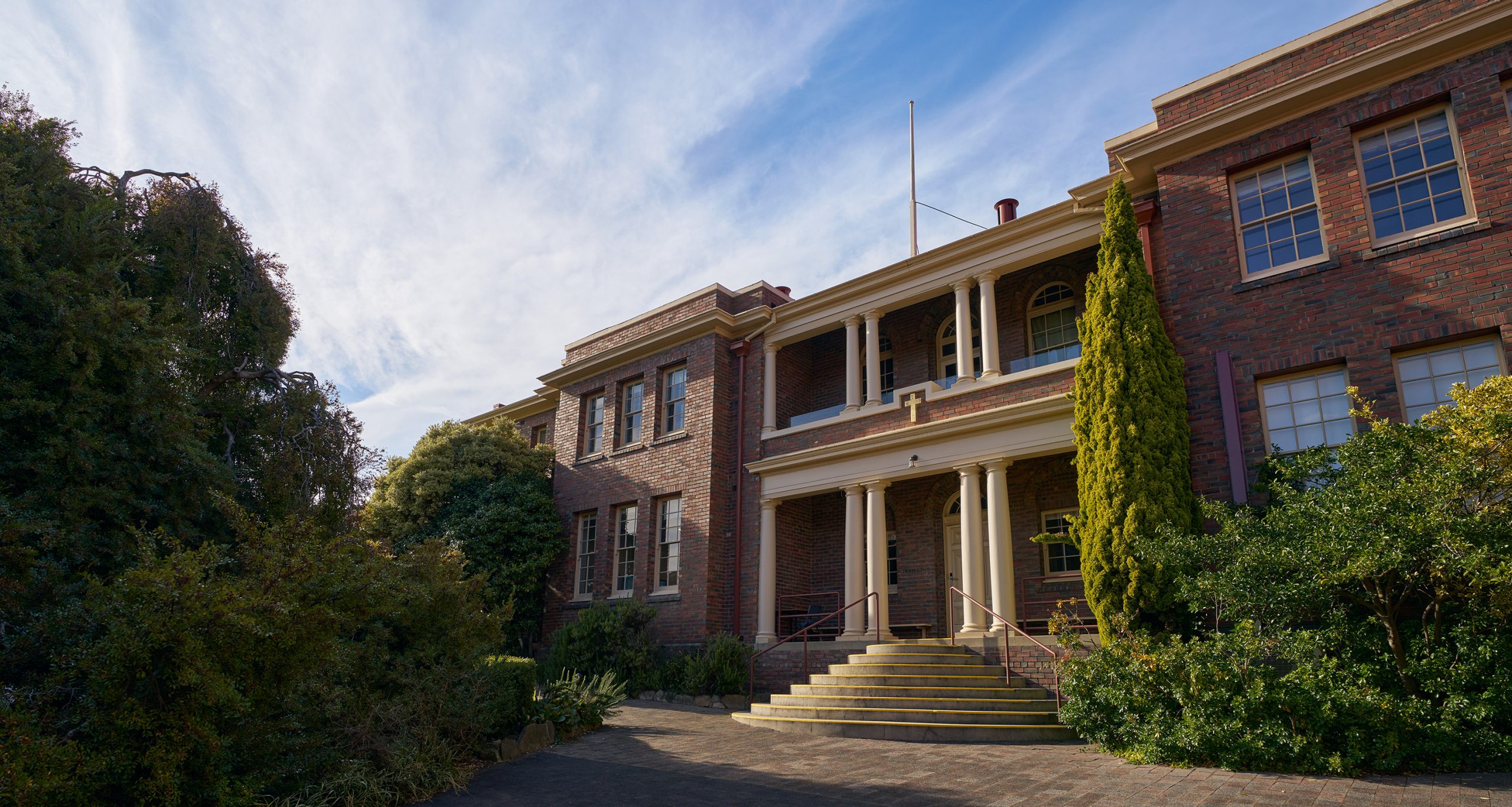An old stately and elegant building surrounded by beautiful gardens and touched by the golden morning sunlight.