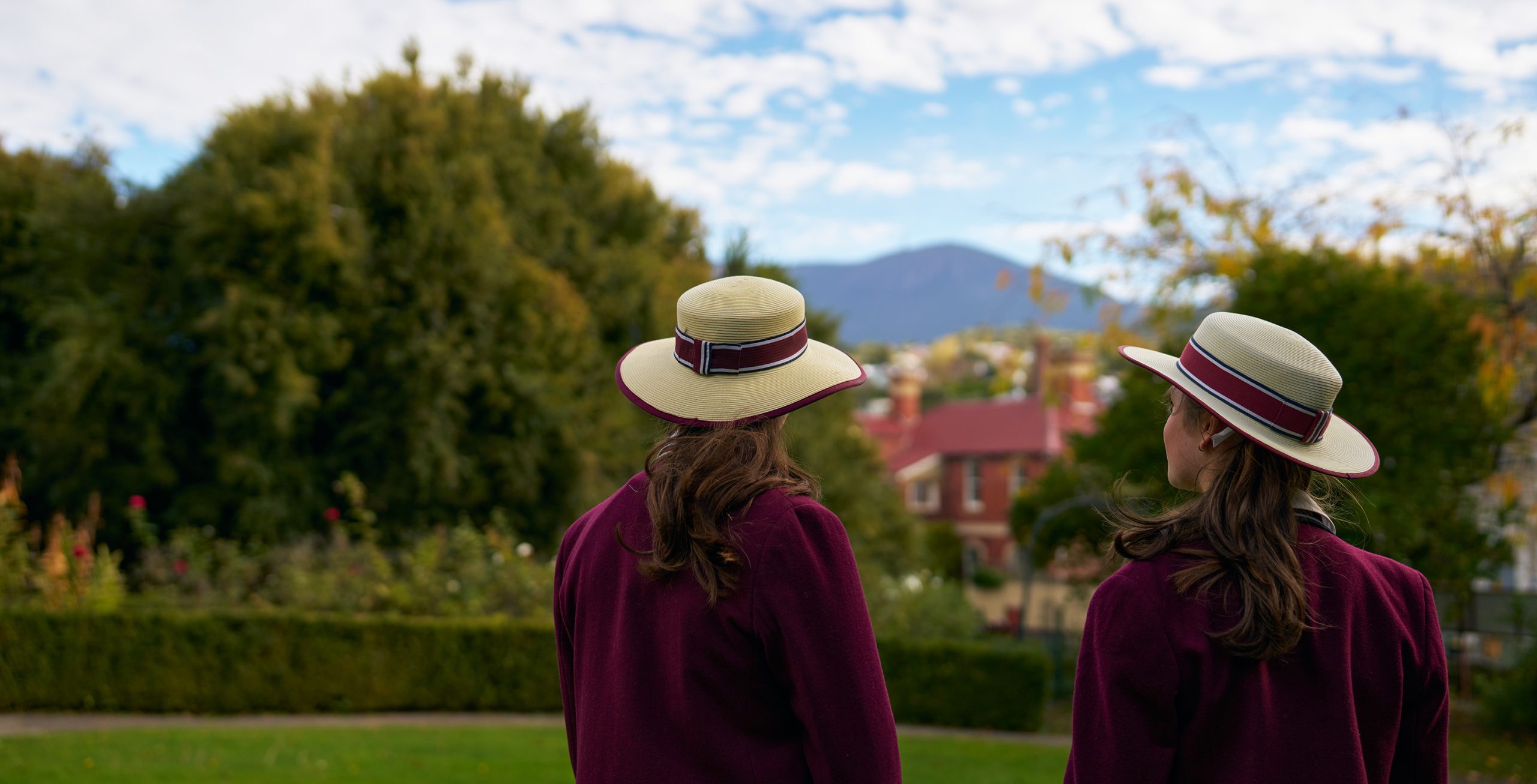 Two students in uniform standing a manicured garden and looking towards the mountain in the distance.